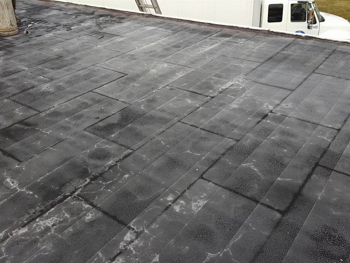 Weathered low-slope roof before repair, with the Seaman Roofing truck on site